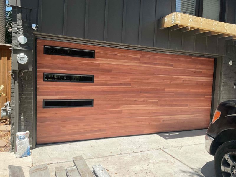A beautiful new wooden garage door against the dark siding of a residential home.