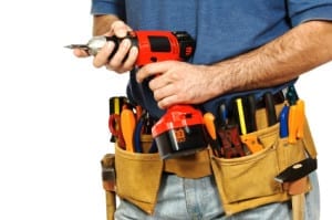 A repair man holding a drill and wearing a tool belt